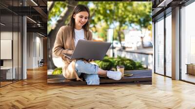 Young beautiful business woman working on a laptop sitting on the bench in the street Wall mural